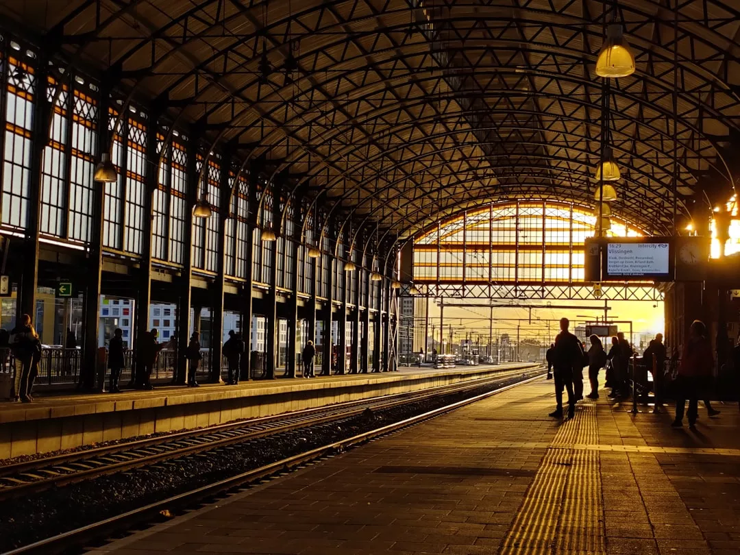 Ein Bahnsteig auf Mallorca bei Sonnenuntergang. Menschen warten unter hohen Bogenfenstern und einer großen Glasdecke, die die Szene in goldenes Licht taucht.