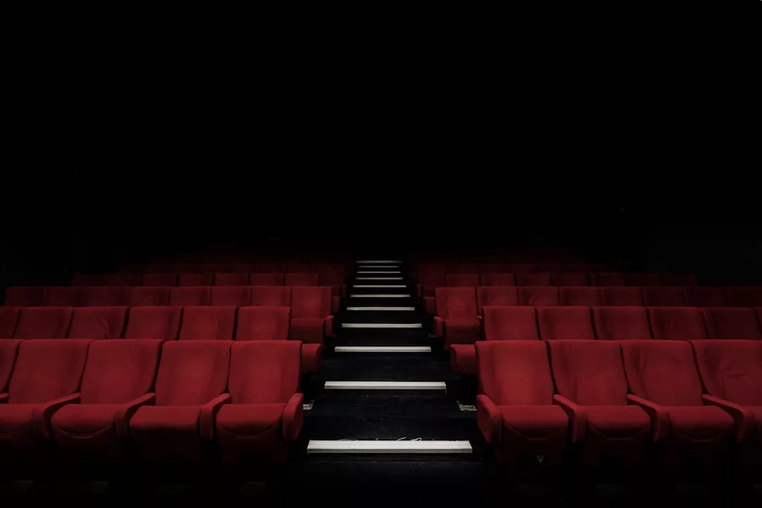 Reihen leerer roter Theatersitze mit Mittelgang und Stufen wecken vor einem dunklen, unbeleuchteten Hintergrund Vorfreude und erinnern an die zeitlosen Veranstaltungsorte auf Mallorca.