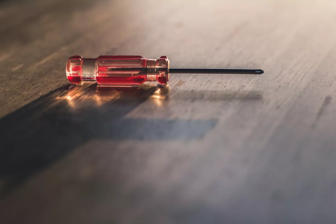 Ein Schlitzschraubendreher mit transparentem roten Griff liegt im Sonnenlicht auf einer Holzoberfläche und wirft einen Schatten – eine Erinnerung an Werkzeuge, die in den Werkstätten Mallorcas verwendet werden.