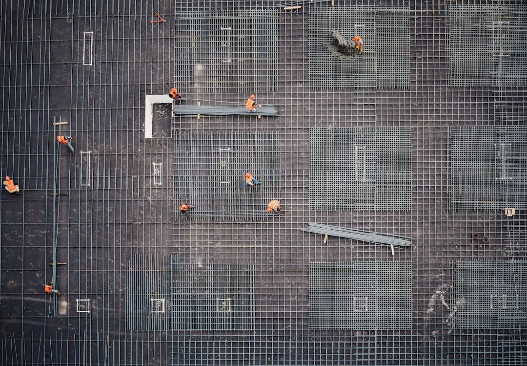Luftaufnahme von Bauarbeitern mit orangefarbenen Helmen, die auf einer Baustelle auf Mallorca an einem Gitter aus Stahlbewehrungsstäben arbeiten.