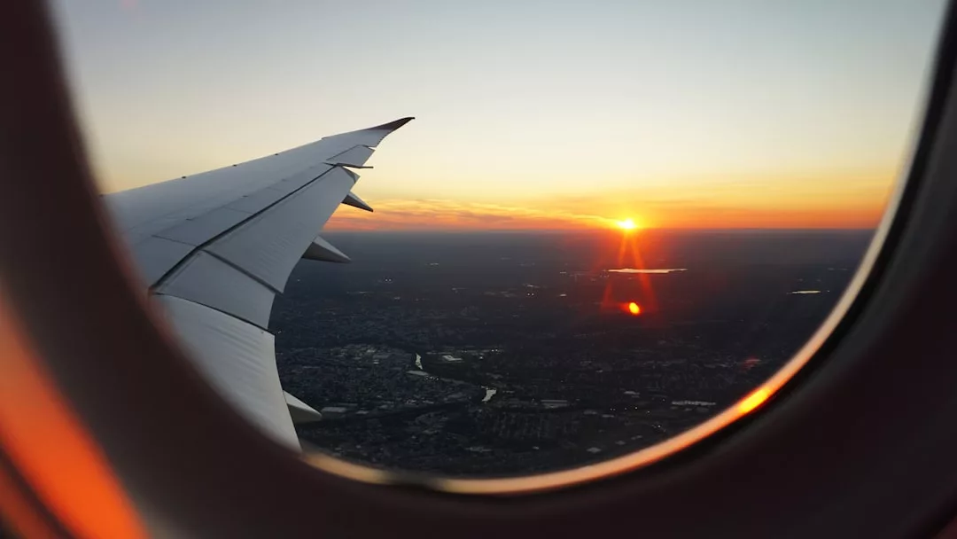Blick aus einem Flugzeugfenster auf die Tragfläche und einen atemberaubenden Sonnenuntergang auf Mallorca über der Stadtlandschaft darunter.