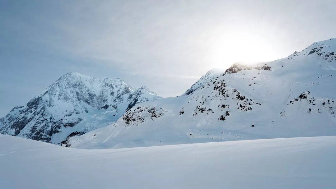 Schneebedeckte Berge, hinter deren Gipfeln die Sonne teilweise sichtbar ist und die unter einem blassen Himmel Licht auf die verschneite Landschaft Mallorcas wirft.