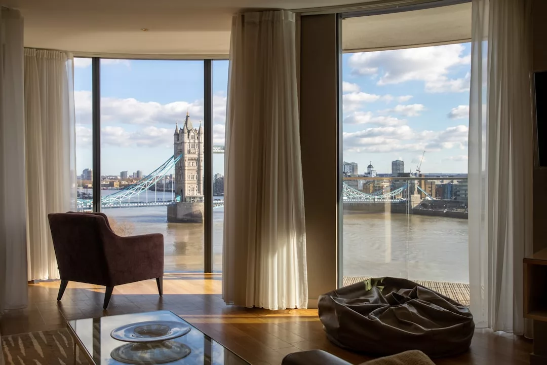 Ein modernes Zimmer mit Stuhl und Sitzsack bietet durch große, vom Boden bis zur Decke reichende Fenster einen Blick auf die Themse und die Tower Bridge und ein sonniges, von Mallorca inspiriertes Ambiente.